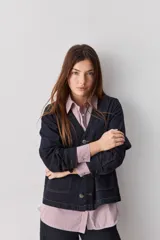 Camisa de calce relajado con diseño a rayas verticales en tonos azul y blanco, cuello clásico, mangas largas con puños abotonados y cierre frontal con botones. Presenta bolsillos aplicados en el delantero y una silueta versátil.