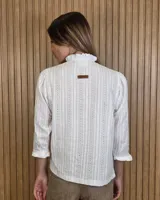 Camisa de algodón color blanco con rayas verticales rosadas, cuello alto con volados, mangas tres cuartos abullonadas con puños elastizados con volados y cierre frontal de botones oscuros.