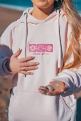 Hoodie rosa con capucha y cordones ajustables. Estampado en la espalda con un diseño de ondas, sol, concha marina y flores de hibisco.