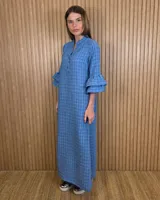 Vestido largo tipo túnica de color azul con estampado a cuadros blancos, cuello mao con escote en V y botones frontales parciales. Presenta mangas tres cuartos con volados en cascada.