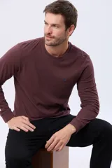 Remera de manga larga con cuello redondo, confeccionada en tejido de algodón con textura jaspeada. Presenta un pequeño logo bordado en el pecho y una etiqueta decorativa en el puño.