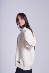 Cárdigan color beige con botones negros, escote en V y detalles de costuras bordadas en negro.