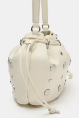 Bolso estilo saca de cuero color marfil, con diseño fruncido en la parte superior, tiras ajustables y tachas metálicas plateadas distribuidas por toda la superficie. Cuenta con una manija superior.