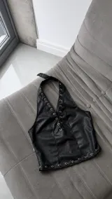 Corset halter de cuero sintético negro con detalles de cordones cruzados en el escote y ojales metálicos en el borde inferior.