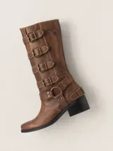 Bota de caña alta estilo biker, color marrón, con punta redondeada y taco cuadrado. Presenta múltiples tiras horizontales con hebillas metálicas y detalles de herrajes en el lateral. Confeccionada en cuero con forro vacuno y suela de madera.