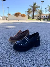 Mocasines de cuero negro con plataforma y suela de goma, decorados con tachas metálicas plateadas en el empeine y el talón.