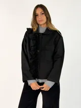 Chaqueta negra de algodón con diseño de volados en el frente, cierre de botones y bolsillos laterales.