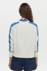 Sweater de punto color blanco con mangas raglán en azul y detalles en verde en los puños, cuello redondo y bordado de libélula en el pecho.