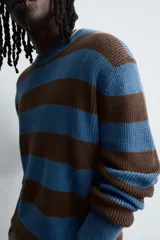 Jersey de punto de algodón con ajuste relajado, cuello redondo y manga larga. Presenta un diseño de rayas horizontales en azul y marrón, con detalles de efecto desgastado y roturas en el cuello, puños y bajo.