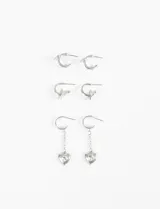 Set de tres pares de aros plateados: un par de argollas lisas, un par de argollas con dije de estrella y un par de aros colgantes con cadena y dije de corazón con piedra de cristal incrustada.