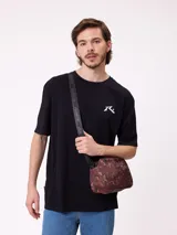 Bolso tipo morral de la marca Rusty, con diseño estampado camuflado en tonos marrones. Cuenta con correa ajustable y cierre frontal con logo de la marca.