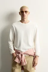 Camiseta relaxed fit de color blanco off-white, confeccionada en tejido texturizado con estructura. Presenta cuello redondo y manga larga.