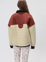 Campera acolchada de diseño colorblock, con el pecho y hombros en tono bordó y el cuerpo y mangas en color beige. Presenta cuello camisero y puños de pana negra, cierre frontal oculto con botones a presión y costuras pespuntadas en patrón cuadriculado.