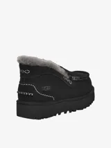 Mule de gamuza color tostado con forro de piel de oveja visible en el borde superior. Presenta costuras decorativas en contraste y una suela de plataforma dentada de goma.