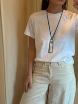 Collar largo con cordón azul, dije rectangular con marco dorado y centro de piedra veteada blanca y gris, y aro dorado.