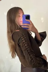 Camisa corta marrón de cuero ovino desgastado, con cuello clásico, cierre frontal con botones, mangas largas con cutouts y puños anchos dorados.