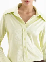 Camisa de jacquard con diseño de flores sutiles, color blanco, con cuello amplio de puntas marcadas, mangas largas con puños y cierre frontal con botones.