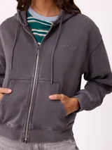 Canguro con cierre frontal y capucha, color gris con efecto desgastado. Presenta bolsillos laterales y logo bordado en el pecho.