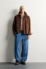 Parka de piel marrón tipo gamuza con cuello solapa, manga larga con puños de botones a presión y múltiples bolsillos de plastrón con solapa en el pecho y la cadera. Cierre frontal de cremallera oculta con solapa.