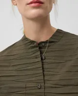 Camisa plisada color verde militar, de cuello redondo y manga larga. Tiene cierre con botones, bolsillo plastrón en el pecho y bajo redondeado.