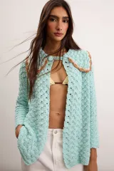 Saco de hilo de algodón tejido a crochet en color celeste, con diseño abierto, mangas largas y cuello romántico con detalles en tono tostado y cierre superior de botón.
