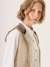 Chaleco de punto con capucha, confeccionado en lana. Presenta un diseño bicolor con cuerpo en tono beige de textura acanalada y capucha en tono marrón. Incluye una etiqueta de cuero en la parte posterior.