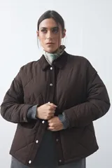 Campera tipo barn capitoneada de color marrón, con silueta corta y relajada. Presenta cuello de pana, cierre frontal con broches metálicos y bolsillos laterales funcionales.