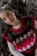 Chaleco tejido de punto con diseño multicolor en bloques, cuello redondo y terminaciones acanaladas. Presenta un patrón geométrico en tonos bordó, rosa, celeste, marrón y crema.