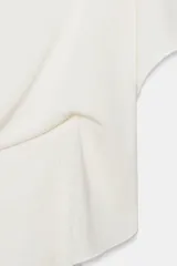 Top tipo capa blanco de punto fluido, con mezcla de viscosa, cuello bote, mangas cortas y bajo asimétrico.