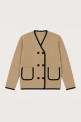 Saco de punto color beige con ribetes en contraste color negro. Presenta un diseño de escote en V, cierre frontal cruzado con botones y dos bolsillos delanteros aplicados.