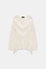 Jersey de punto color blanco roto, manga larga, con cuello redondo y detalle de encaje en el delantero en forma de volados en 'V'. El bajo es asimétrico.