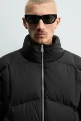 Cazadora acolchada de corte relajado confeccionada en tejido técnico color verde militar. Presenta cuello subido, cierre frontal con cremallera, mangas largas con puños elásticos y bolsillos frontales con cremallera oculta.