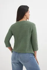 Cardigan verde esmeralda de tejido de punto calado, con mangas 3/4 y corte evasé. Presenta cuello redondo con abertura en forma de gota y cierre con un único botón.