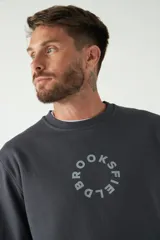 Buzo de felpa color beige con cuello redondo, manga larga y puños acanalados. Presenta un logo circular estampado en el frente.