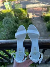 Sandalias de cuero blanco con taco bajo, tira delantera simple, talón cerrado y pulsera ajustable al tobillo con hebilla dorada.