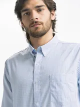 Camisa celeste y blanca a cuadros con cuello abotonado, manga larga y bolsillo en el pecho.