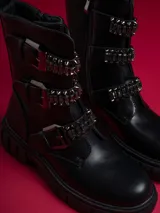 Botas negras de caña baja con suela track, cierre lateral y detalles de hebillas con tachas y cadenas.