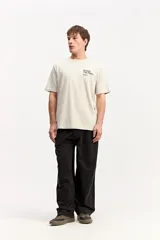 Remera de manga corta color beige, con estampa en la espalda que incluye un paisaje marino de atardecer y texto.