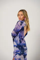 Vestido largo con estampado abstracto en tonos azul, lila y blanco. Tiene cuello mao con abertura en forma de lágrima, mangas largas acampanadas, espalda abierta, tajo frontal y flecos en el ruedo.