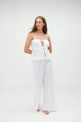 Top de pijama blanco confeccionado en algodón, con tirantes finos, escote recto y aberturas frontales con lazos ajustables.