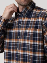 Camisa de manga larga con estampado de cuadros, confeccionada en algodón orgánico cepillado. Presenta cuello clásico, cierre frontal con botones de madera y dos bolsillos en el pecho.