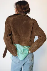 Cazadora corta de ante color marrón, con cuello de solapa, cierre frontal cruzado con cremallera, mangas largas con cremalleras en los puños y bajo con cinturón ajustable.