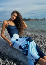 Vestido largo de corte ajustado, confeccionado en tela elastizada de color azul oscuro con un estampado floral abstracto en tonos blancos que recorre el lateral de la prenda. Presenta escote redondo y breteles finos.