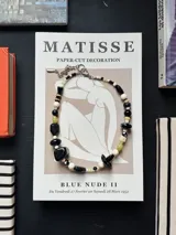Collar de cuentas artesanales con piedras en tonos negro, blanco, beige y verde claro, combinadas con abalorios de diferentes formas y tamaños, y cadena de ajuste metálica con cierre de mosquetón.