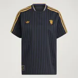 Camiseta de fútbol Adidas del Manchester United, modelo Terrace Icons. Diseño negro con sutiles rayas verticales moradas, franjas amarillas en los hombros y detalles bordados en dorado, incluyendo el trébol de Adidas y el escudo clásico del club.