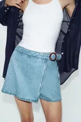 Falda pantalón cruzada de denim en color celeste, con diseño cruzado al frente, cierre frontal oculto y hebilla decorativa redonda en la cintura.