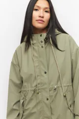 Piloto verde militar de manga larga con capucha y forro de color amarillo. Cuenta con dos bolsillos laterales con solapa, cordones ajustables, elástico en los puños, cierre y botones metálicos.