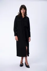 Vestido camisero midi negro con cuello camisero, mangas largas, dos bolsillos en el pecho, cinturón de lazo y abertura lateral.