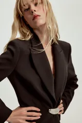 Blazer entallada de cuello solapa y manga larga con hombreras. Presenta bolsillos delanteros de vivo y cierre frontal con un botón metálico decorativo.