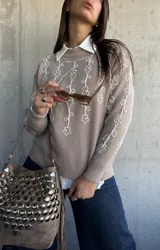 Sweater de punto color beige con bordado de flores blancas en el frente y las mangas, cuello redondo y puños acanalados.